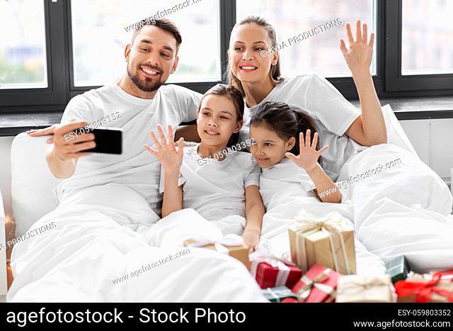 family with christmas gifts taking selfie in bed