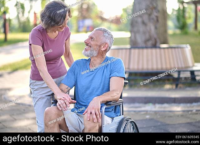 In the park. A man in a wheel chair and his wife on a walk in the park