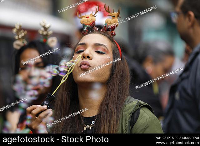 15 December 2023, Venezuela, Caracas: A woman blows soap bubbles in the poor district of Petare during the gift handover of the ""A toy, good news"" campaign