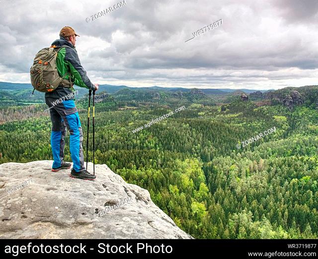 The body of man with a backpack and running shoes stands on top of a rock against the background rocky valley high in the mountains