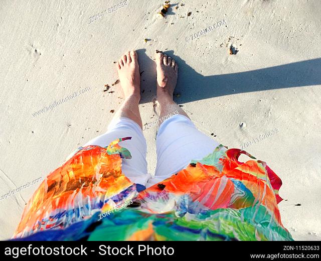 Sand covered feet and legs on the beach in early morning light with long shadows. POV looking down
