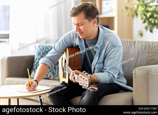 man with guitar writing to music book at home