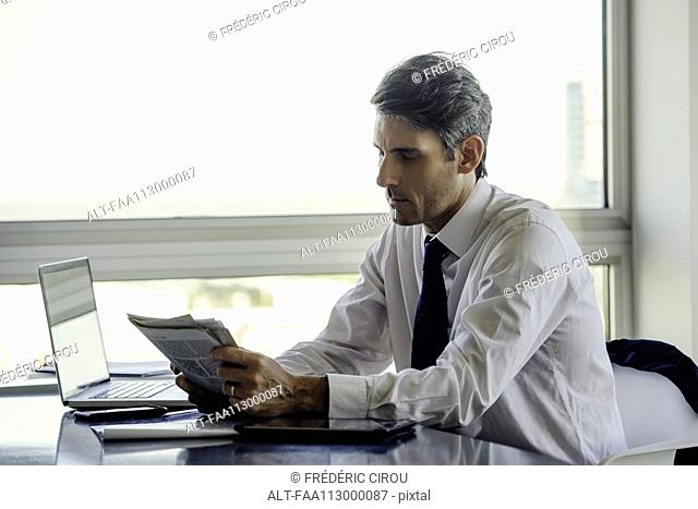Man reading newspaper in office