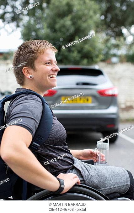 Happy young female university student in wheelchair in parking lot