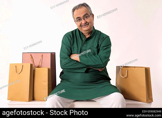 AN OLD MAN LOOKING AT CAMERA WHILE SITTING WITH SHOPPING BAGS