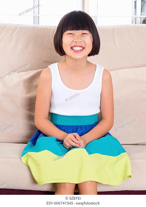 Seven years old Southeast Asian child sitting on sofa at home with happy face