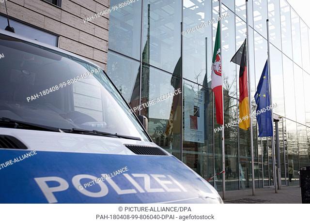 08 April 2018, Germany, Muenster: Flags flying at half-mast behind a police van. A man drove in to a group of people in front of a restaurant on 07 April and...