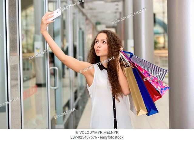 beautiful young woman goes shopping using a smartphone with a shopping bags in the mall