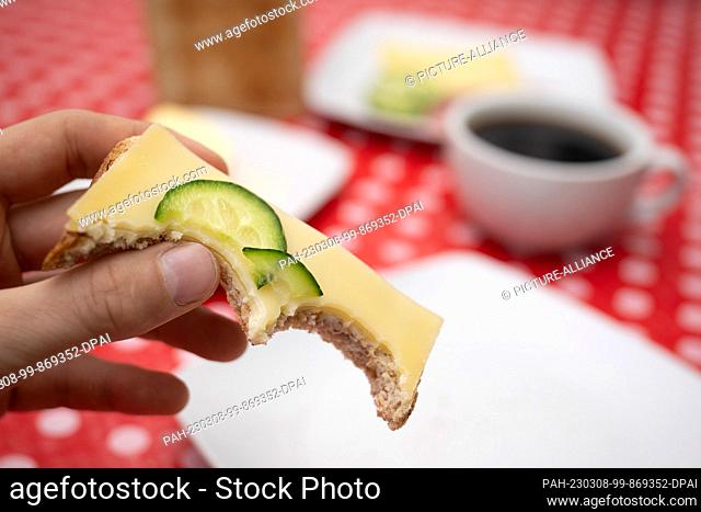 ILLUSTRATION - 06 March 2023, Hesse, Gießen: A man holds a piece of toast with cheese. When asked about the ""most important meal"" of the day