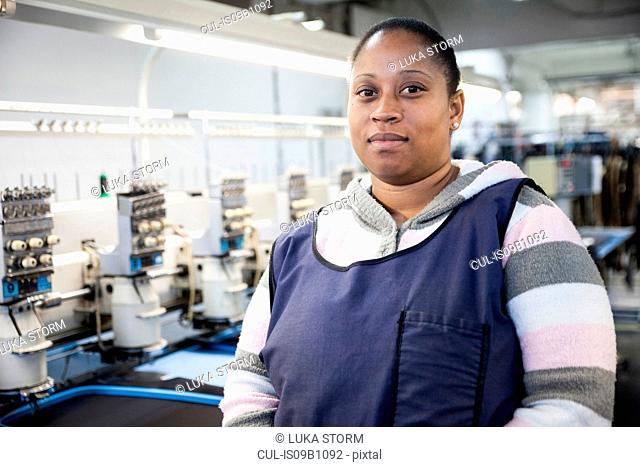 Portrait of female factory worker in front of programmed embroidery machines in clothing factory