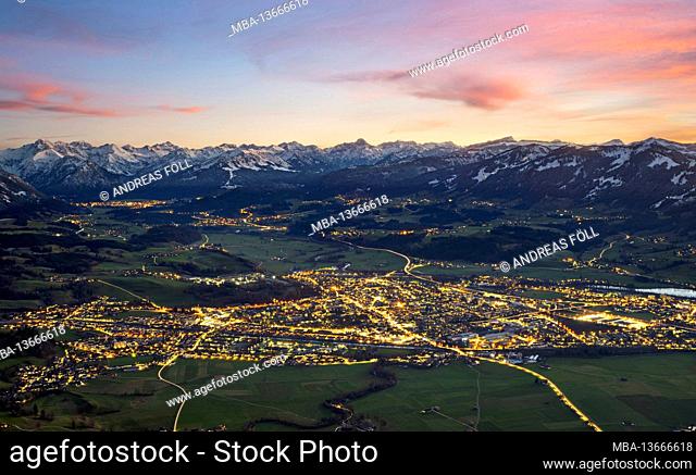 Illertal illuminated at dusk from Sonthofen to Oberstdorf. Framed by the snow-capped Allgäu Alps under a blue sky and glowing red clouds