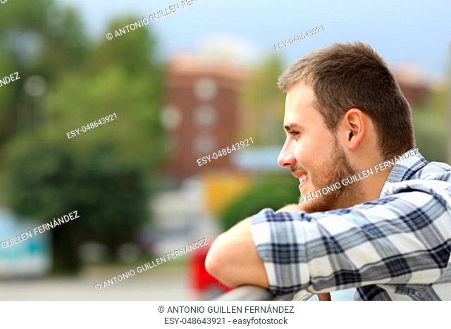 Side view of a happy man looking away and enjoying urban views from a balcony of a house or hotel