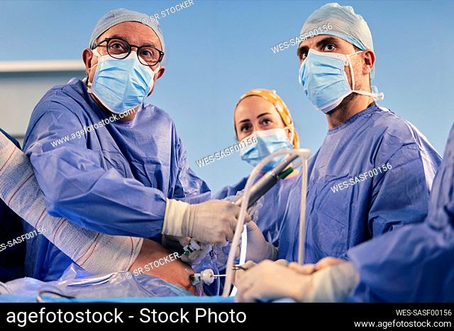 Surgeons wearing protective face mask operating shoulder arthroscopic surgery while standing in operation room during COVID-19