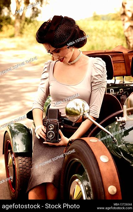 Young 1940s style woman with vintage car in British racing green and old camera