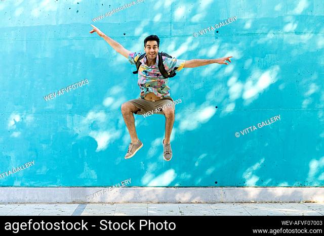 Casual man jumping in front of blue wall