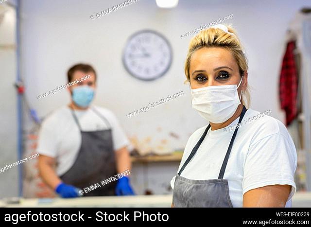 Mid adult woman wearing face mask standing with coworker in background at workshop