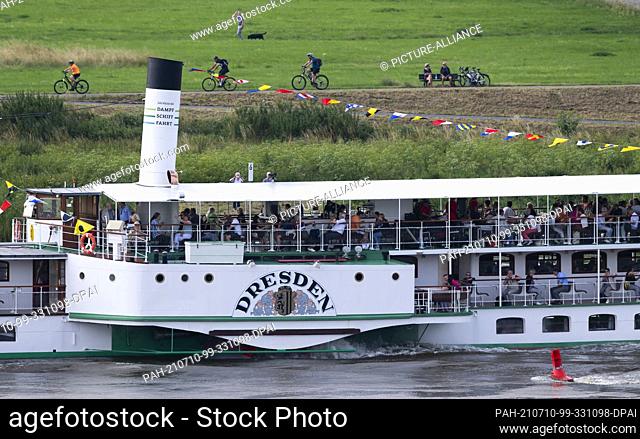 10 July 2021, Saxony, Dresden: Cyclists, strollers and the steamer ""Dresden"" filled with excursionists can be seen during the steamer parade between...