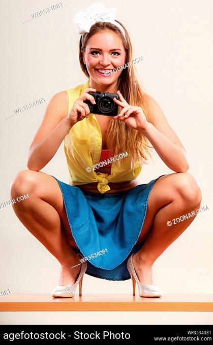 Happy smiling pretty pin up girl wearing hairband bow, skirt and high heels taking photo picture with camera. Attractive gorgeous young retro woman...