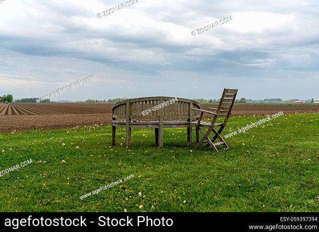 Empty wooden garden furniture on a green field under an overcast sky with a freshly plowed field behind