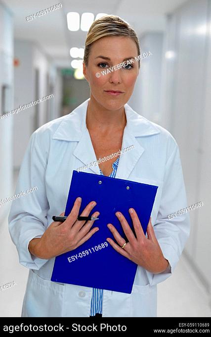 Portrait of caucasian female doctor standing in hospital corridor holding medical chart document
