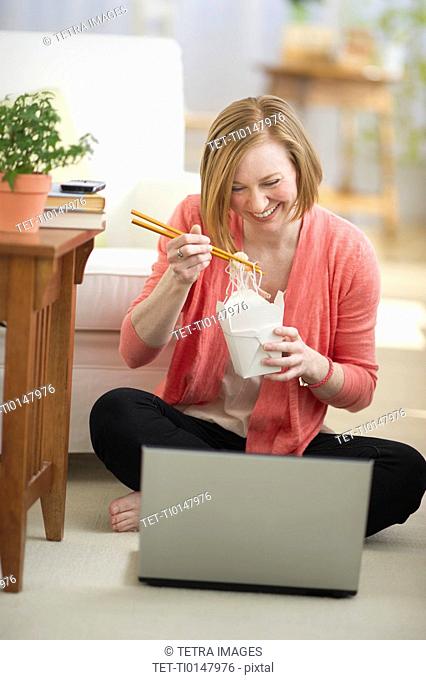 USA, New Jersey, Jersey City, woman sitting on floor, using laptop and eating take out food