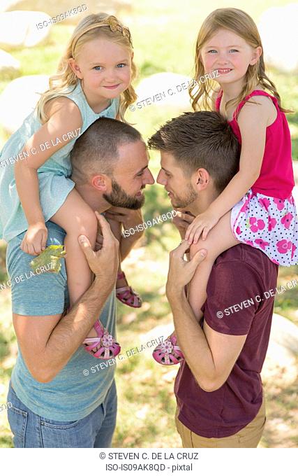 Two sisters sitting on both fathers shoulders in park