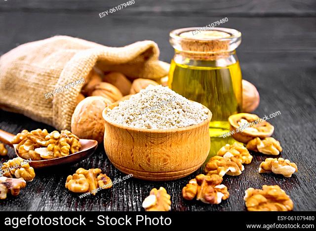Walnut flour in bowl, nuts on a table, in a spoon and in a bag, oil in glass jar on wooden board background