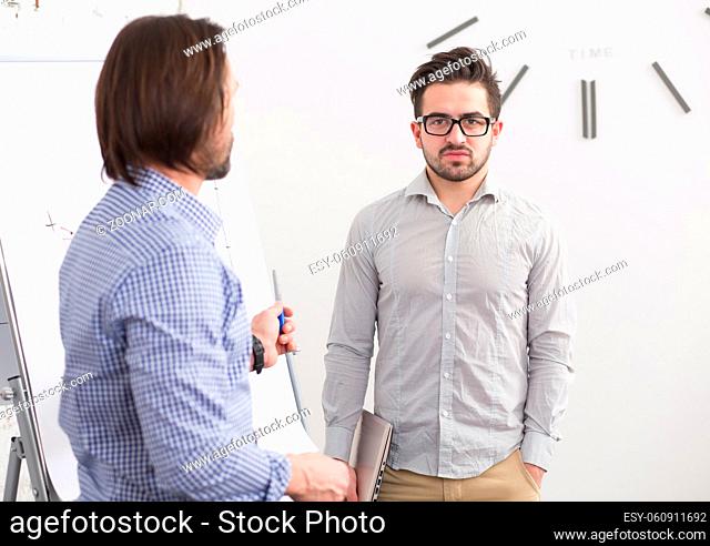 Portrait of two businessmen in office communicating. Business man with quite long hair telling something to his colleague