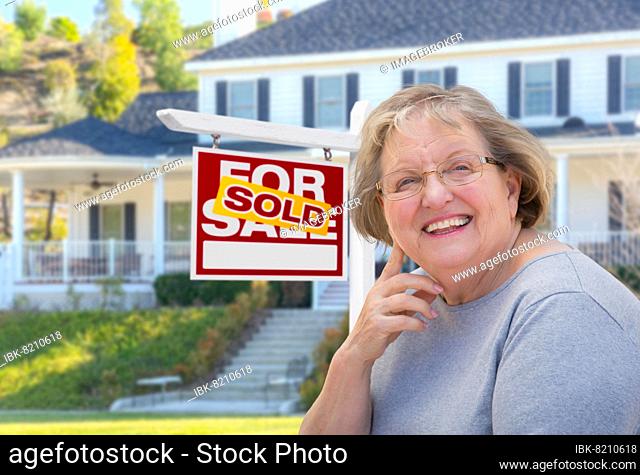 Senior adult woman in front of sold home for sale real estate sign and beautiful house