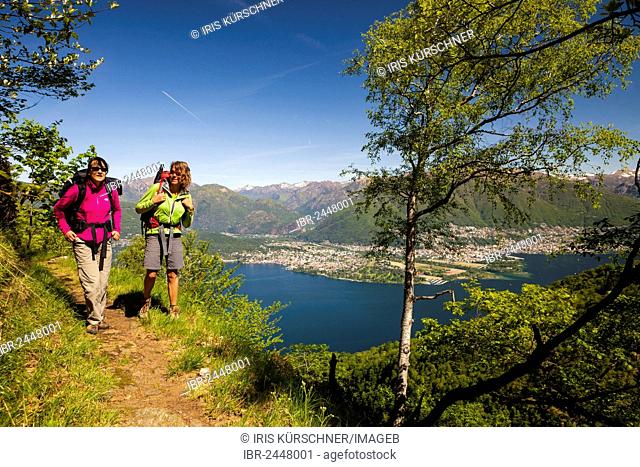 Two women hiking on the high trail of Monti di Vairano to Monti Caviano on Monte Gambarogno, overlooking the Maggia delta, Ascona and Locarno, Ticino
