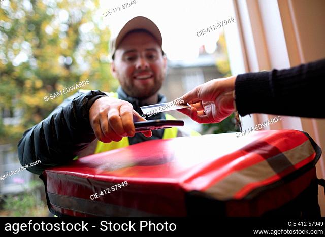 Customer paying delivery man with contactless card at front door