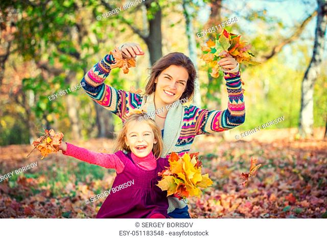 Little girl and her mother playing with bright autumn leaves in the autumn park