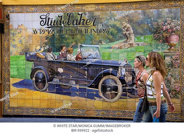 Girls passing a wall of tiles depicting a Studebaker car in Calle Tetuan street, Seville, Andalusia, Spain, Europe