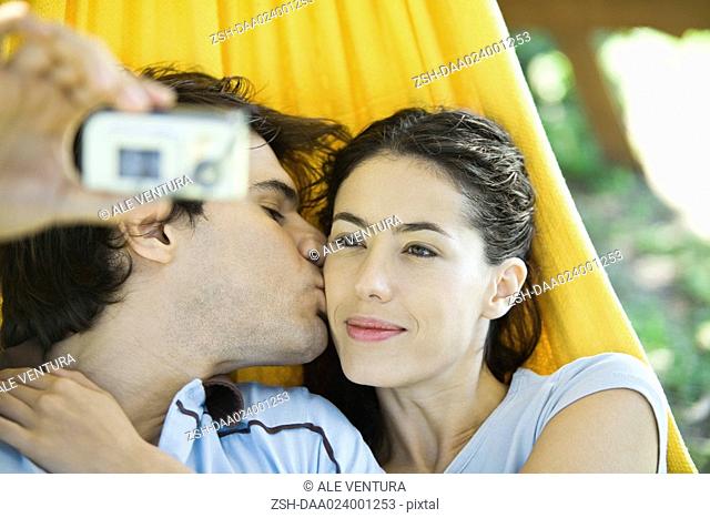 Young couple lying in hammock, taking photo of selves with digital camera