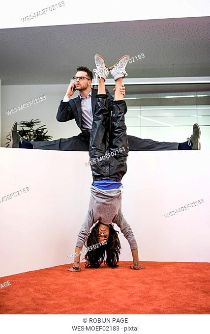 Businessman in office holding woman's legs doing a handstand