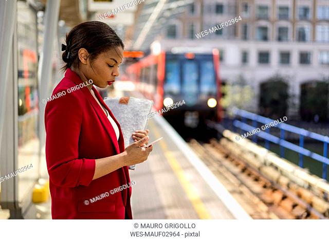 Businesswoman standing on platform looking at mobile phone, London, UK