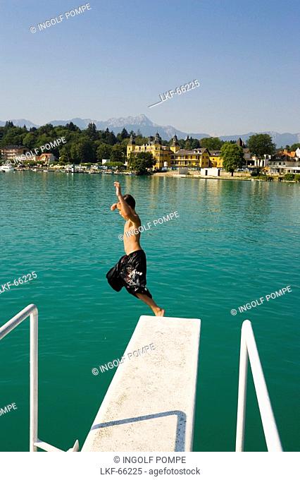 Boy jumping from diving platform into Woerthersee biggest lake of Carinthia, Hotel Schloss Velden served as the location for the TV series Ein Schloss am...