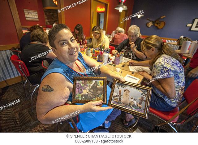 Women of different ages gather at an adult coloring book workshop at a Lake Forest, CA, restaurant function room as a woman proudly shows off her finished work