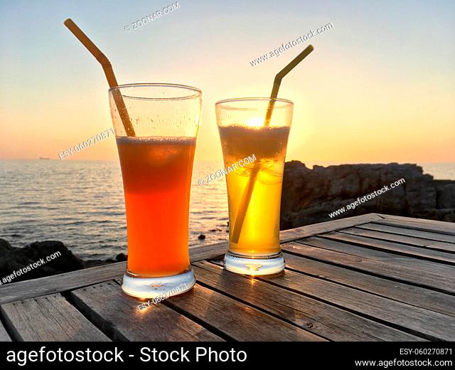 Frozen cocktail glasses with straws on wooden table over sea sunset