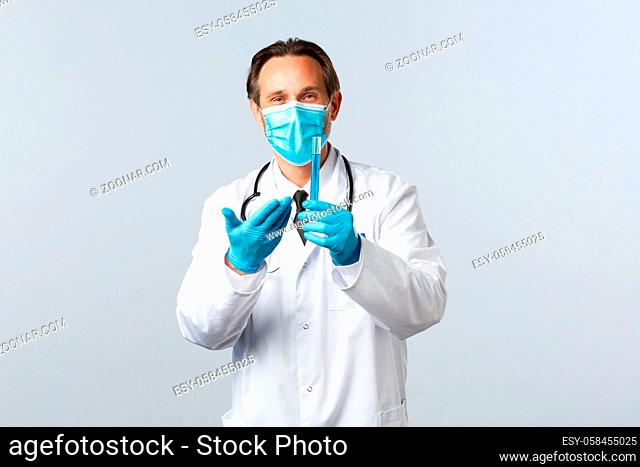 Covid-19, preventing virus, healthcare workers and vaccination concept. Satisfied smiling doctor in medical mask and gloves pointing at test-tube with vaccine...