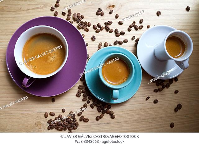 White porcelain cups, cyan and magenta with expresso coffee, on wooden board decorated with roasted coffee beans