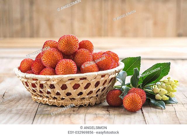 Basket with ripe arbutus unedo fruits, leaves and floers on a wooden background