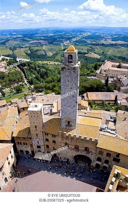 People in the Piazza del Duomo with the town's oldest tower of the Palazzo Vecchio Podesta built in 1239 with the farmland east of the town beyond