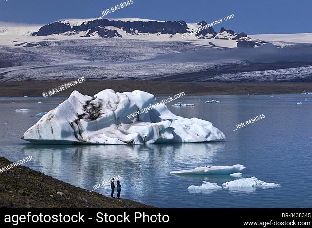 Two people in front of an iceberg at Jökulsarlon glacier lagoon, Vatnajökull National Park, Hornarfjördur, Iceland, Europe