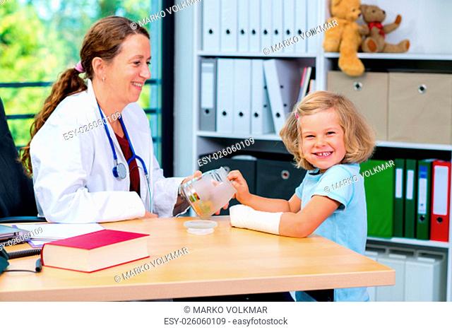 female pediatrician in white lab coat has candys for a little girl