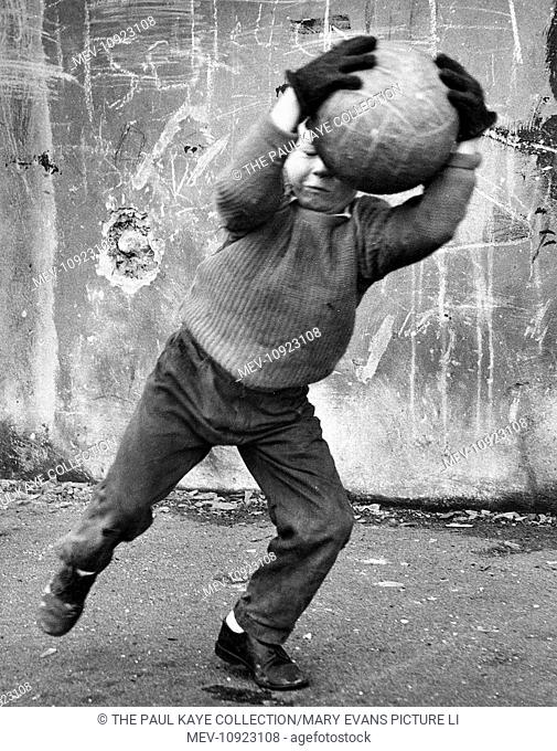 Small boy catching a football in front of a concrete wall in a street in Balham, SW London