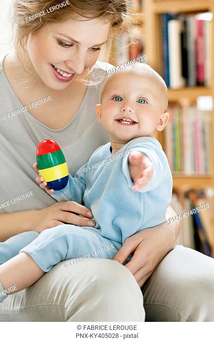 Baby girl sitting on the lap of her mother playing with a toy