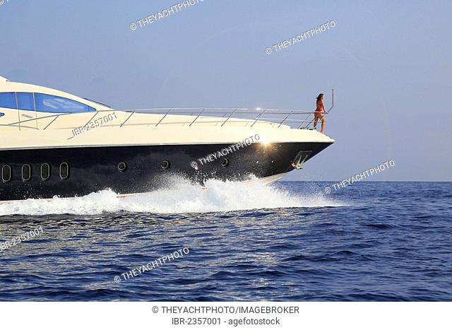 Young woman wearing a red swimsuit standing on the bow of a moving motor yacht, French Riviera, Cote d'Azur, Mediterranean Sea, Europe