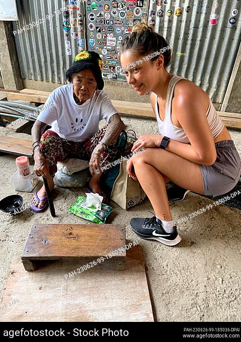 PRODUCTION - 24 May 2023, Philippines, Buscalan: British tourist Jade Kühnl (26, r), gets a tattoo from Maria Oggay, known as Apo Whang-Od