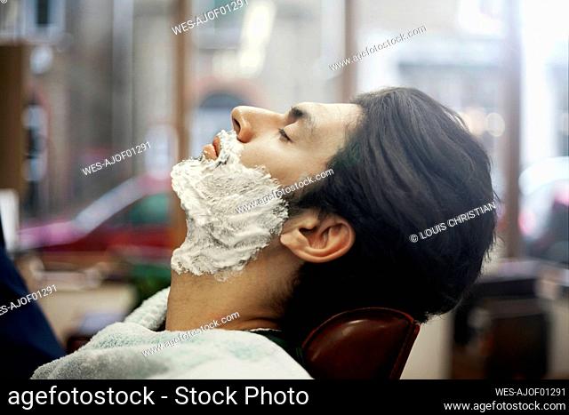 Profile of male customer sitting in barber shop with shaving cream on face